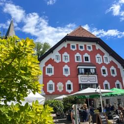 Red and white Rathaus building in Saalfelden with outdoor café terrace. Green foliage frames the traditional Austrian architecture under blue sky.