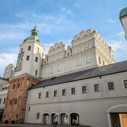 Courtyard of the Castle of the Pomeranian Dukes showing white Renaissance facades with ornamental gables, a tower with green dome, and arched passages.