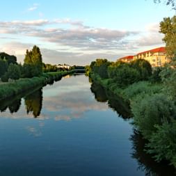 Ruhige Havel spiegelt bewölkten Himmel wider, gesäumt von grüner Vegetation und Wohngebäuden zu beiden Seiten zur goldenen Stunde.