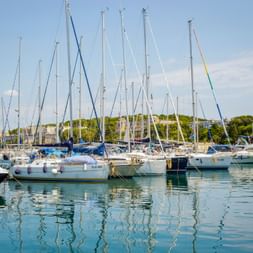 Yachthafen in Pula, Istrien mit zahlreichen Segelbooten am Steg. Klares türkisfarbenes Wasser spiegelt die weißen Masten unter blauem Himmel.