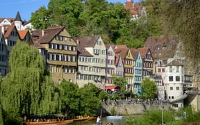 Bunte Fachwerkhäuser säumen den Neckar in Tübingens Altstadt. Traditionelle Holzboote mit Menschen treiben auf dem Wasser.