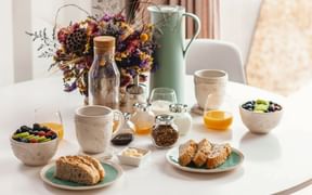Breakfast table laid, plates with slices of bread, orange juice, coffee cups, fruit bowls