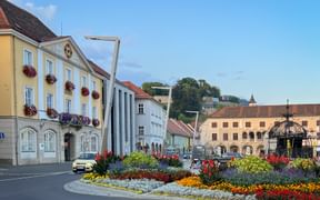 Historischer Hauptplatz in Bruck an der Mur mit bunten Barockgebäuden, verziertem Pavillon und rundem Blumenbeet mit leuchtenden Blüten.