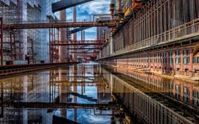 Historic coal mine Zeche Zollverein with red brick buildings, steel structures and water reflections creating mirror image of industrial architecture.