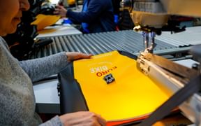 Arbeiter näht gelbes Eurobike Satteltaschen-Material unter industrieller Nähmaschine in Produktionsstätte.