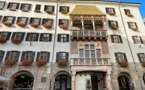 Historic Innsbruck building with the famous Golden Roof balcony featuring ornate frescoes and golden tiles, surrounded by colorful flower boxes.