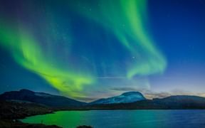 Grüne Aurora Borealis tanzt über den Nachthimmel über einem See und Bergen im Abisko Nationalpark, Schweden.