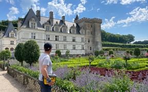 Cyclist with helmet viewing a French Renaissance castle along the Loire cycle route. Ornamental gardens with colorful flowers in foreground.
