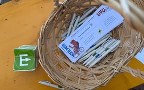 Wicker basket containing white pens and Eurofun vouchers on wooden table. Green stickers with white arrow symbols are placed beside the basket.