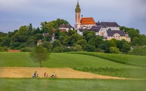 Das Kloster Andechs, umgeben von Wiesen und Feldern, im Vordergrund eine Radfahrgruppe
