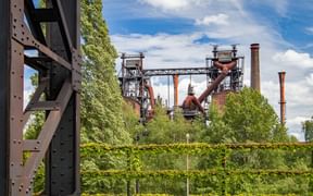 Former industrial complex at Landschaftspark Nord in Duisburg with blast furnaces, smokestacks and steel structures surrounded by green vegetation.