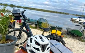 Bicycle with white helmet and yellow panniers at Lech reservoir. Boats and calm water visible in background under cloudy sky.