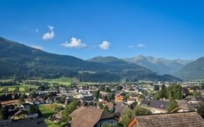 Panoramablick auf das Dorf St. Michael im Lungau in einem Alpental mit traditionellen Häusern, grünen Wiesen und bewaldeten Bergen.