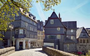 Steinbrücke führt zu Wetzlars historischer Altstadt mit traditionellen deutschen Fachwerkhäusern und Schieferdächern unter blauem Himmel.