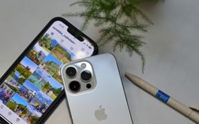 Two smartphones on white surface displaying social media content with cycling photos, alongside green plant and wooden pen.