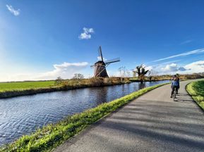 Radfahrer am Radweg neben Windmühle und Rhein