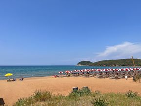 Baratti beach with red and white parasols against a blue sky