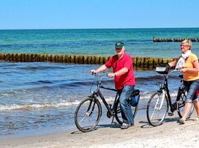 Radfahrer die ihr Rad am Strand entlang schieben in Nordfriesland