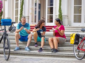 Two women and a man take a break from cycling on the steps of the Merano Kurhaus with an ice cream in their hands