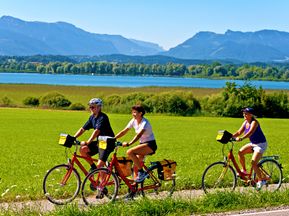 Drei Radfahrer mit Chiemsee und den bayerischen Alpen im Hintergrund