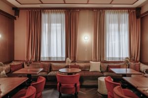 Elegant breakfast room with coral-pink tones, wooden tables, upholstered seating, and draped windows at Parkhotel Mondschein in Bozen.