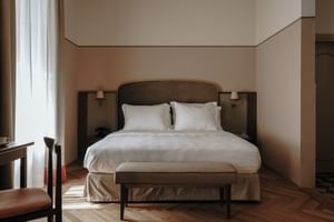 Modern hotel room with double bed, white linens, dark headboard, wooden floor, and beige walls at Parkhotel Mondschein in Bolzano.