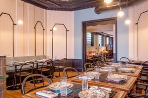Modern restaurant interior with set tables, metal chairs, decorative ceiling, and white paneled walls with geometric frames at Hotel Labé Tours.