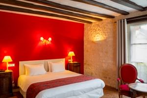 Hotelzimmer mit Holzbalken, roter Akzentwand, weißem Bett, Steinwand und traditioneller Einrichtung im Le Grand Monarque in Azay-le-Rideau.