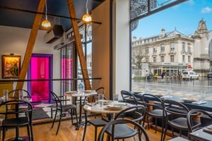 Contemporary bar interior with black bistro chairs, round tables, exposed wooden beams, and floor-to-ceiling windows overlooking a Tours street.