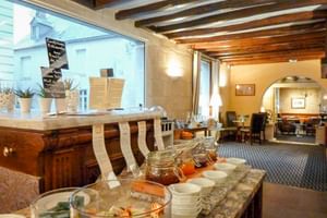 Frühstücksbuffet im Le Grand Monarque in Azay-le-Rideau mit Marmeladen, Brot und Geschirr auf Steintheke. Sichtbare Holzbalken und Speisesaal.