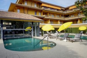 Yellow hotel building with balconies and outdoor pool area with sun loungers and yellow umbrellas at Du Lac et Bellevue in Bardolino.