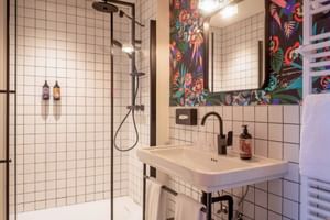 Hotel Labé Tours bathroom with white tiles, glass shower, black fixtures, and vibrant floral wallpaper around mirror above sink.