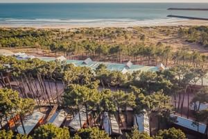 Aerial view of FeelViana Sport Hotel in Viana do Castelo with modern buildings among pine trees, sandy beach, and Atlantic Ocean in background.