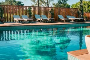 Outdoor pool with turquoise water at FeelViana Sport Hotel Cabedelo. Six sun loungers with cushions line the wooden deck behind a fence.