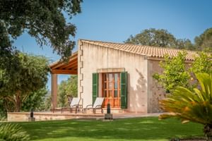 Steinhaus der Finca Son Roig mit Terrakottadach, grünen Fensterläden und überdachter Terrasse, umgeben von Rasen und mediterraner Vegetation.