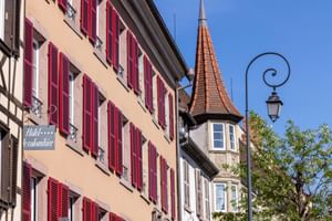 Hotel Le Colombier in Colmar mit traditioneller elsässischer Architektur mit roten Fensterläden, Fachwerkfassade und mittelalterlichem Turm.