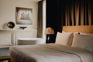 Modernes Doppelzimmer im The Dean Munich Hotel mit weißem Bett, freistehender Badewanne, Kupferlampe und dunklen Vorhängen.