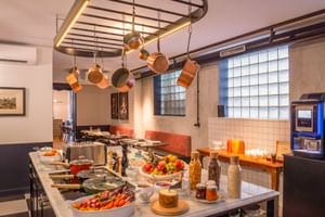 Breakfast buffet at Hotel Labe Tours with fresh fruit, vegetables, cereals, and beverages on a marble counter under a hanging pot rack.