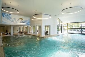 Modern indoor pool with turquoise water at Du Lac et Bellevue Bardolino. Large circular pendant lights hang from the ceiling above the pool.