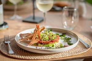 Elegante Vorspeise mit Thunfisch-Tartar, Avocado, Microgreens und knusprigem Brot auf weißem Teller im Restaurant Son Roig, serviert mit Weißwein.