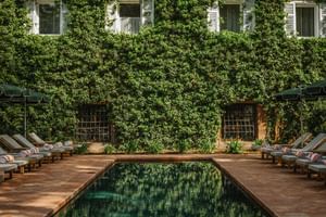 Outdoor pool at Parkhotel Mondschein Bozen with wooden deck, sun loungers, and ivy-covered building facade with white shuttered windows.