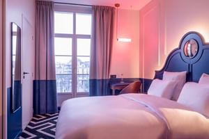 Modern double room with pink and blue decor, featuring a bed with decorative headboard, French doors, and geometric floor pattern.