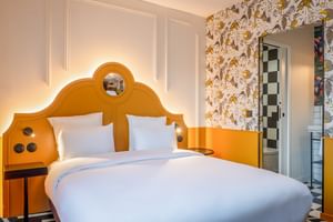 Modern double room with distinctive orange curved headboard, white bedding, floral wallpaper, and en-suite bathroom at Hotel Labe Tours.