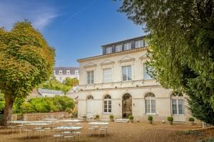Elegantes cremefarbenes Herrenhaus Le Grand Monarque in Azay-le-Rideau mit Bogenfenstern und Außenterrasse mit weißen Tischen und Stühlen.
