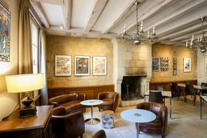 Elegante Bar-Lounge mit sichtbaren Balken, Steinwänden, braunen Ledersesseln, weißen Tischen, Kamin, Kronleuchtern und Kunstwerken im Le Grand Monarque.