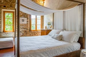 Double room with white canopy bed, stone walls, terracotta floors, and wooden windows at Agriturismo Le Valli in Casciana Terme, Tuscany.