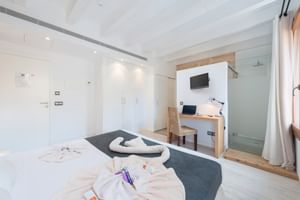 Modern hotel double room with white bed, wooden desk area, glass shower, built-in wardrobes and contemporary design in neutral tones.