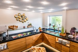Frühstücksbuffet mit Holztheken, Glasabdeckungen, Brotkörben, frischem Obst, Aufschnitt und Kaffeestation im Gartenhotel Heusser.