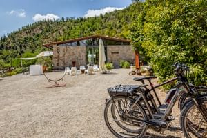 Stone building with terrace and white sun loungers at Agriturismo Le Valli in Casciana Terme. Bicycles parked on gravel courtyard, hills in background.