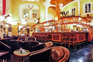 Elegante Hotelbar mit Holztresen, Ledersitzgruppen, gelben Wänden, Jagdtrophäen und Rundbogenfenstern im Salzburger Hof Bad Gastein.
